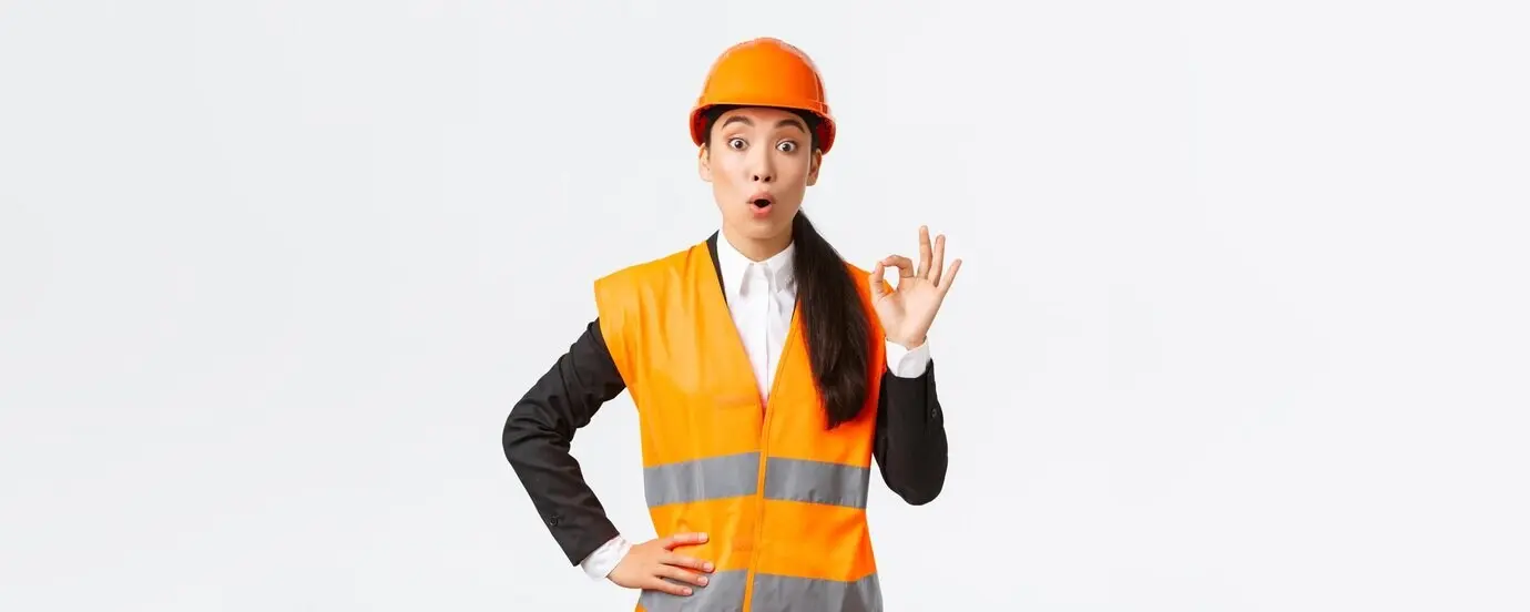 Mujer asiática, gerente de construcción, impresionada y sorprendida, complacida con la asombrosa calidad, de pie con casco de seguridad y chaqueta reflectante, mostrando el gesto de OK y diciendo “wow”, con fondo blanco.